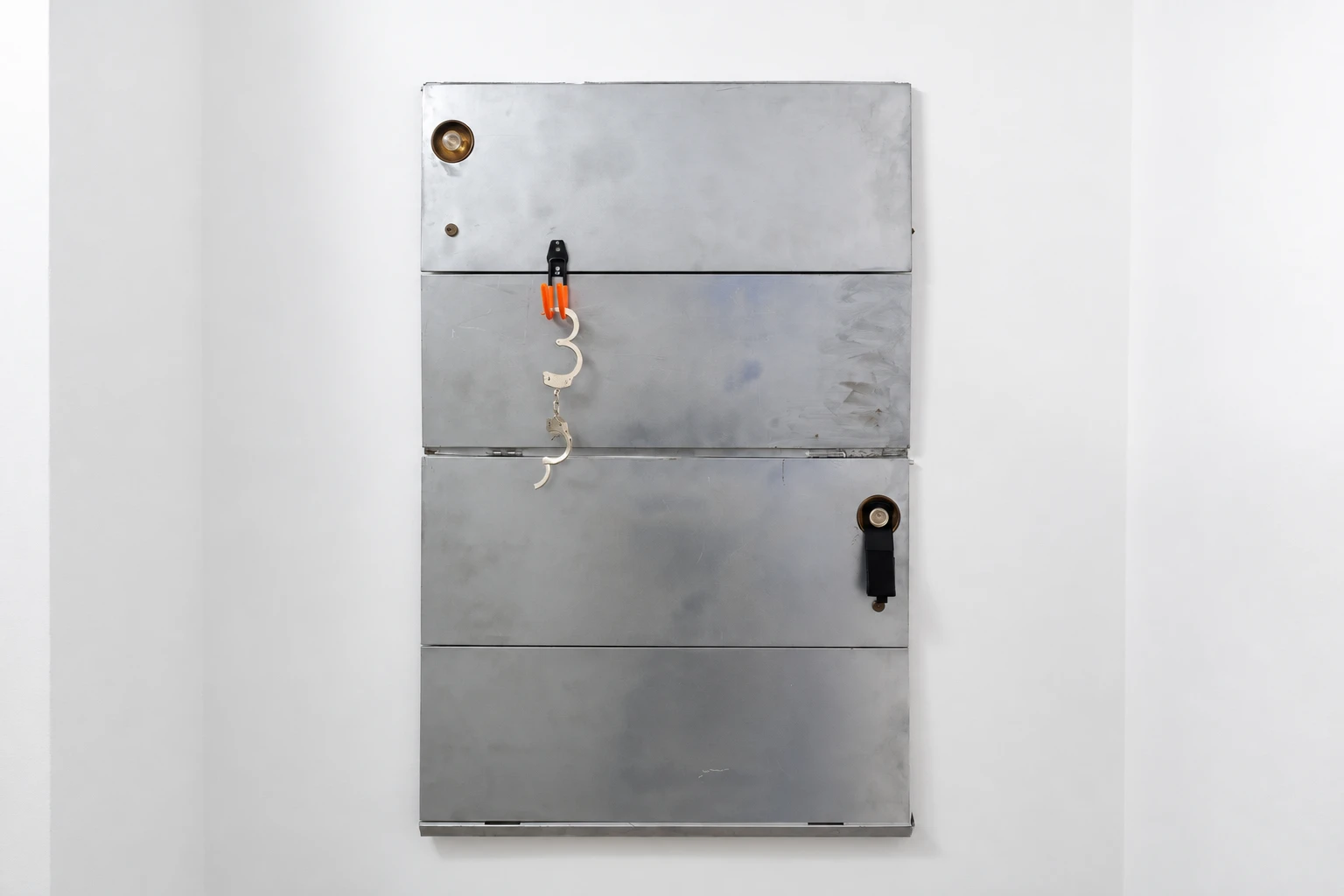 Silver-painted steel cabinet doors mounted on a wall, with an orange hook and broken handcuffs; complete work in landscape view