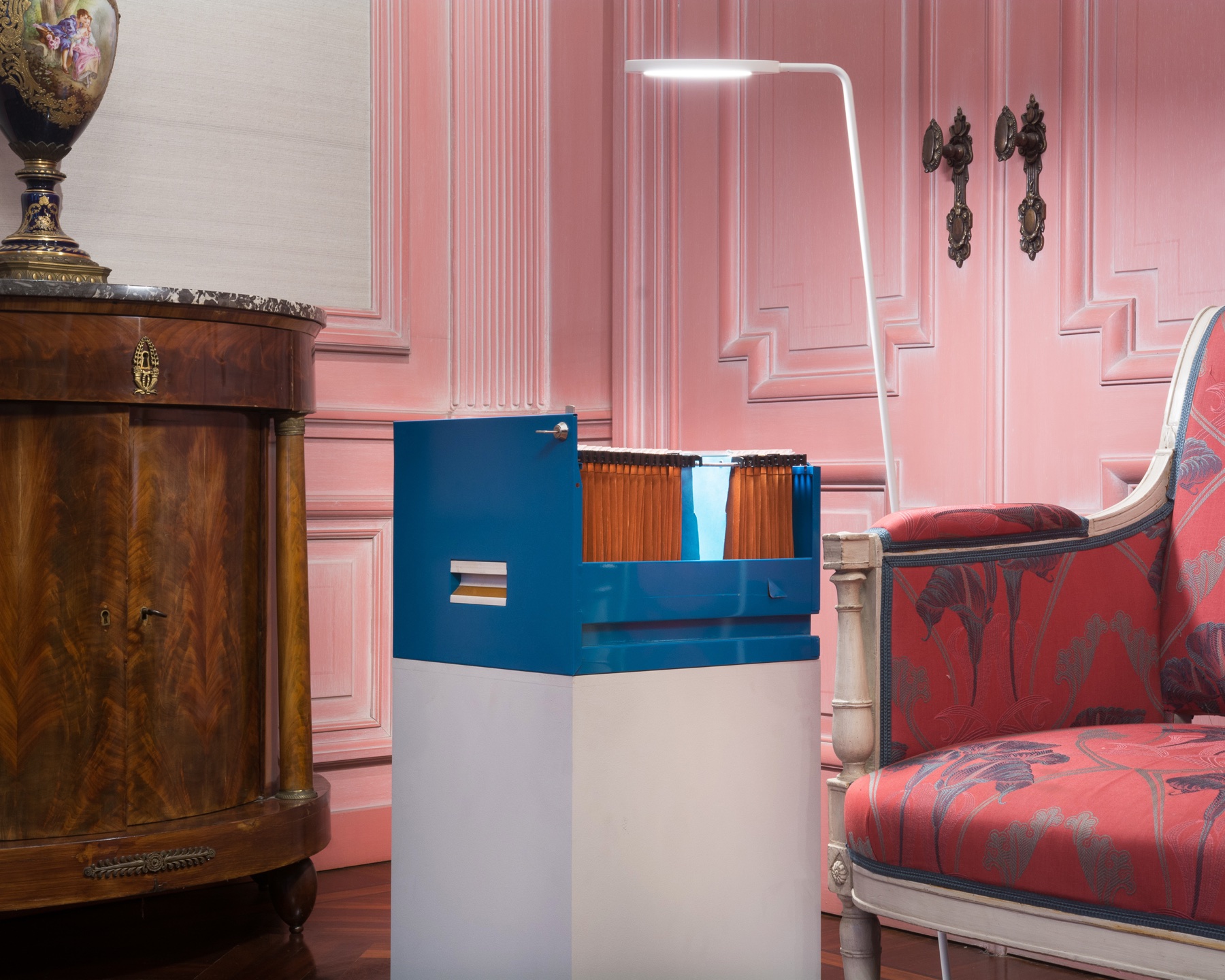 Blue filing cabinet and plinth lit inside a furnished room